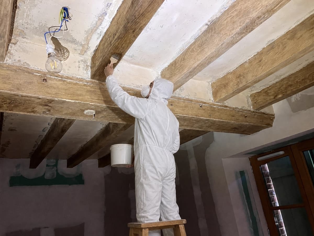 Traitement au pinceau d'une poutre en chene sous un plafond partiellement restaure